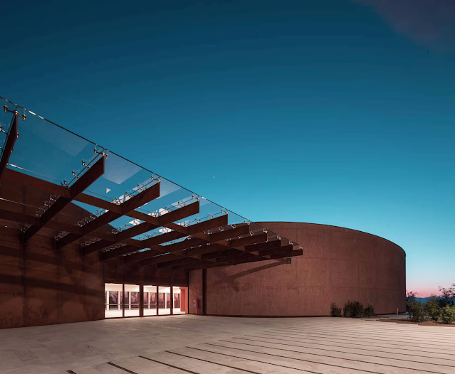 Forum Bertarelli front entrance with glass canopy at dusk.